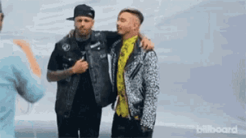 two men are standing next to each other and one of them is hugging the other .