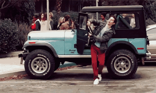 a man is getting out of a blue jeep that says bfgoodrich on the tires .