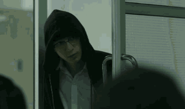 a man wearing glasses and a hooded jacket is standing in a doorway .