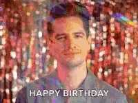 a man is standing in front of a wall of confetti and says happy birthday .