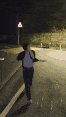 a person is running down a street at night with a triangle sign in the background .
