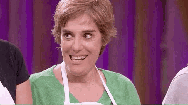 a woman in a green shirt and apron is smiling on a stage .