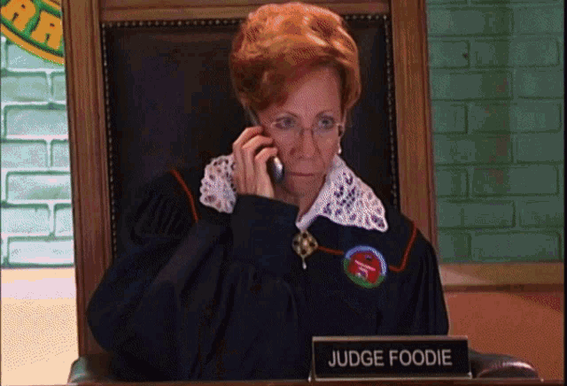 a woman in a judge 's robe is sitting at a desk with a sign that says judge foodie