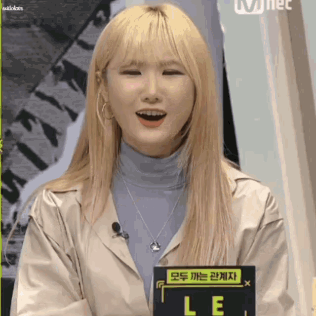 a woman with blonde hair is holding a sign that says le on it