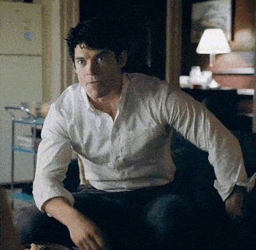 a man in a white shirt is sitting on a couch in front of a refrigerator