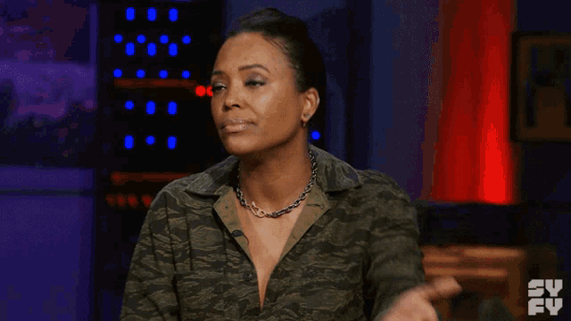 a woman wearing a camo shirt is sitting in front of a tv screen
