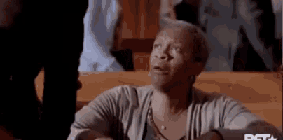 an elderly woman is sitting in a church with her eyes closed and making a funny face .
