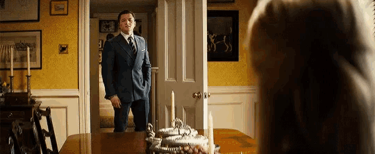 a man in a suit and tie is standing in a dining room next to a table .