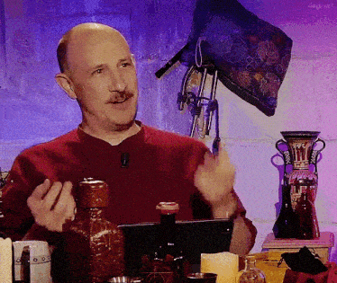 a bald man with a mustache is sitting in front of a table with bottles and a tablet ..