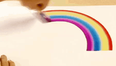a person is drawing a rainbow on a piece of paper with a brush .