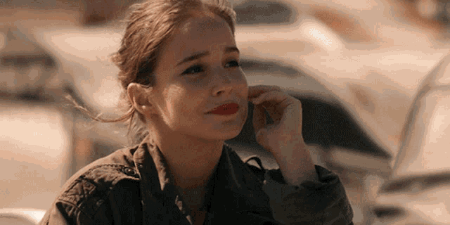 a woman wearing a green jacket and red lipstick is sitting in front of a car