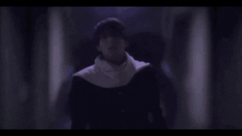 a man is standing in a dark hallway wearing a white scarf around his neck
