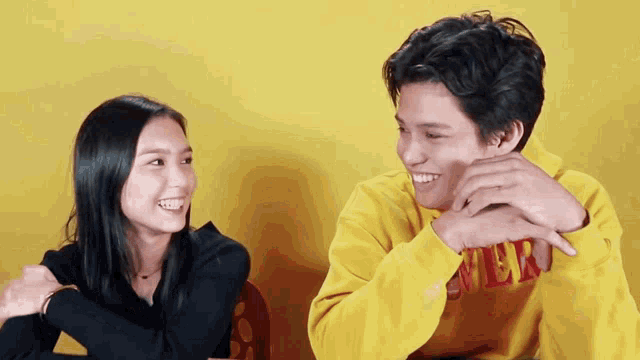 a man wearing a yellow sweater with the word ver on it is smiling next to a woman