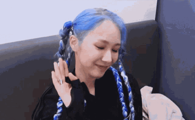 a woman with blue hair is sitting on a couch and smiling