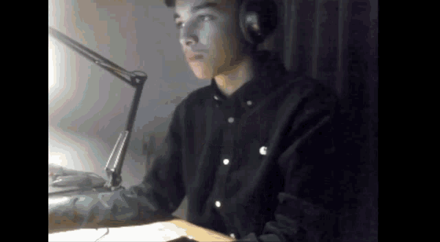 a young man wearing headphones sits at a desk in front of a microphone