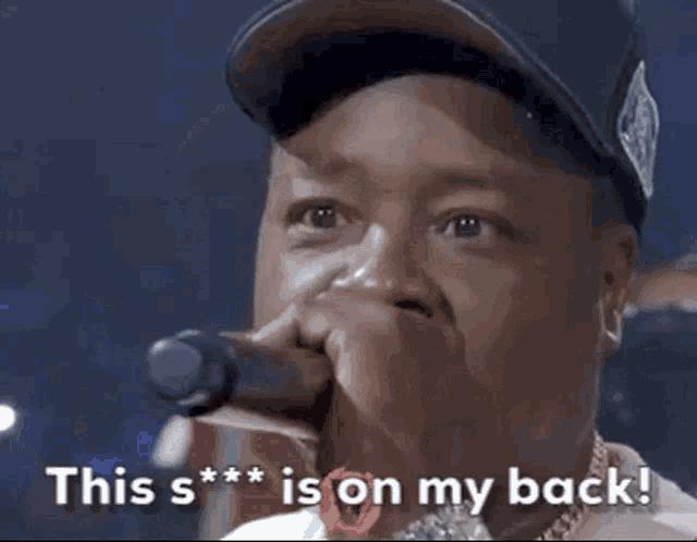 a man is holding a microphone in front of his mouth and saying `` this s *** is on my back '' .