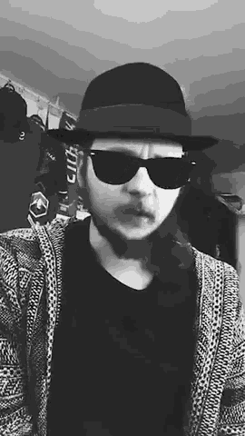 a black and white photo of a man wearing a fedora and sunglasses