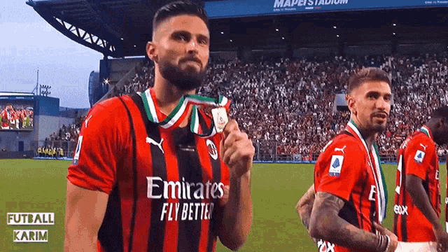 a soccer player wearing an emirates fly better jersey holds a medal