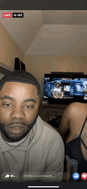 a man is sitting in front of a television with a live 141 notification on his phone screen