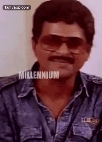 a man with a mustache and sunglasses is wearing a denim shirt and making a funny face .