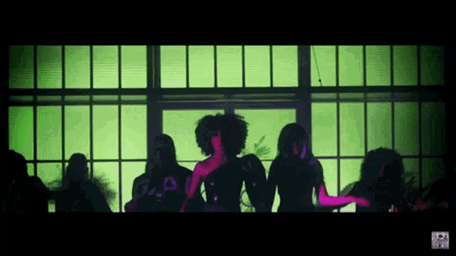 a group of people are standing in front of a window with a green light behind them
