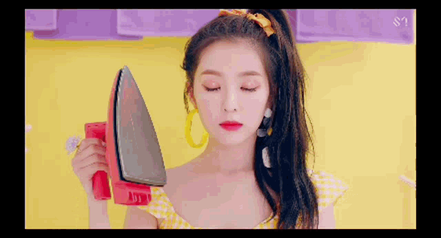 a woman in a yellow dress is holding a red iron in her hand .