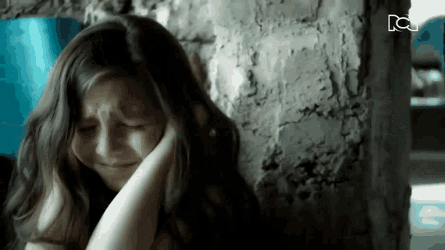 a girl covering her ears in front of a brick wall with the letters nc on it