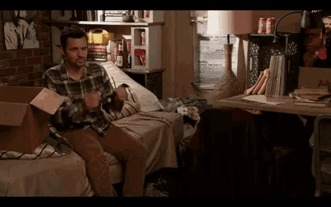a man in a plaid shirt is sitting on a bed with a cardboard box