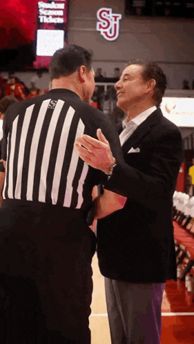 a man in a suit shakes hands with a referee wearing a jersey that says sj on the back