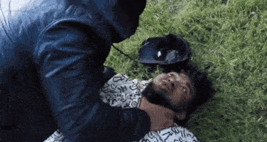 a man in a blue jacket is holding another man 's neck while laying in the grass .