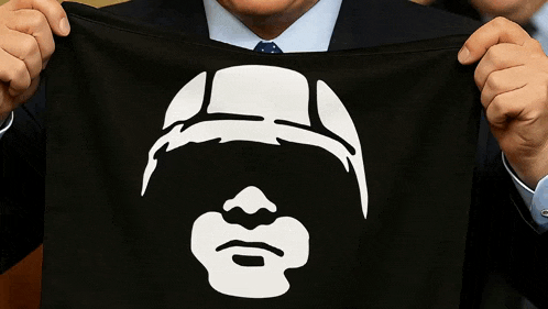 a man in a suit and tie holds a black cloth with a white face on it