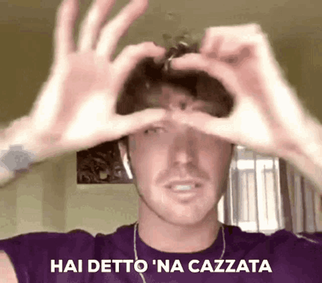 a man wearing a purple shirt is making a heart shape with his hands .
