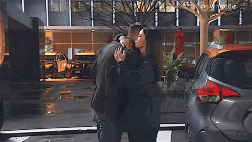 a man and a woman are hugging in front of a car that says nissan