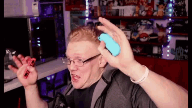 a man wearing glasses is holding a blue nintendo switch controller .
