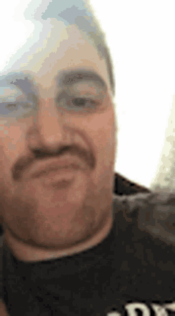 a man with a mustache is making a funny face while wearing a black shirt .