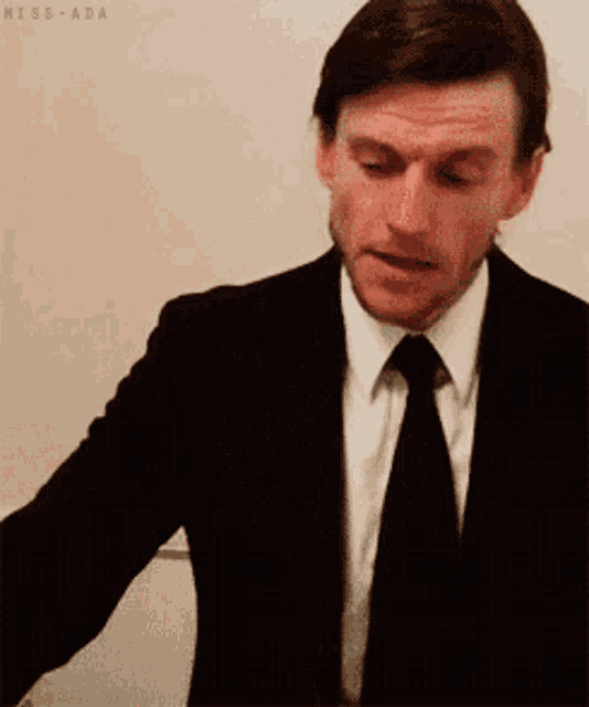 a man in a suit and tie is standing in front of a white board that says miss-ada on it