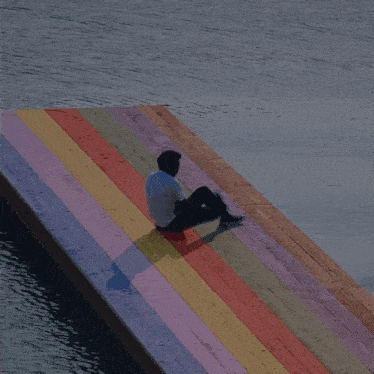 a man sits on a colorful wooden dock overlooking a body of water