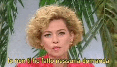 a woman with blonde curly hair is standing in front of a palm tree and says lo non ti ho fatto nessuna domanda .