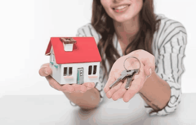 a woman is holding a small house and keys
