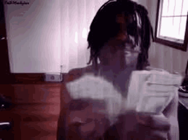 a man with dreadlocks is holding a bunch of money in his hands in a room .