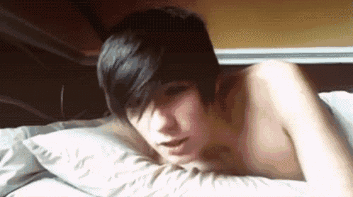 a shirtless young man with short black hair is laying on a bed with a pillow .