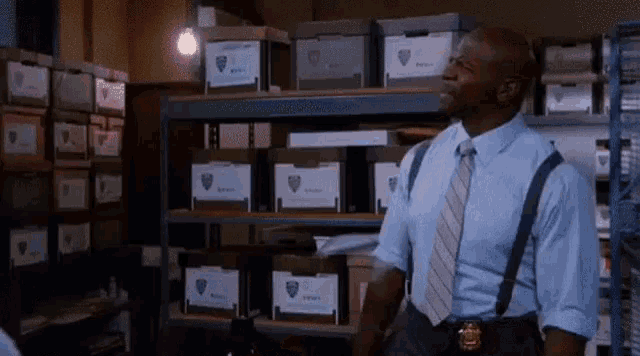 a police officer in a blue shirt and tie is standing in a room filled with boxes .