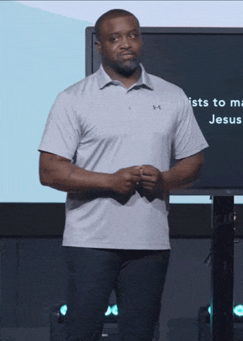 a man in an under armour shirt stands in front of a large screen