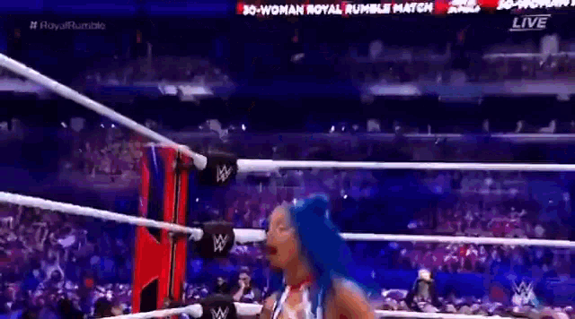 a woman with blue hair is standing in a wrestling ring with a crowd watching .