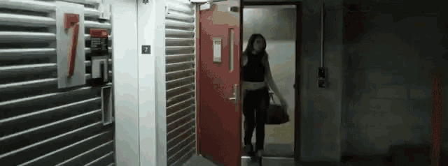 a woman in a black top and black pants is walking through a doorway .