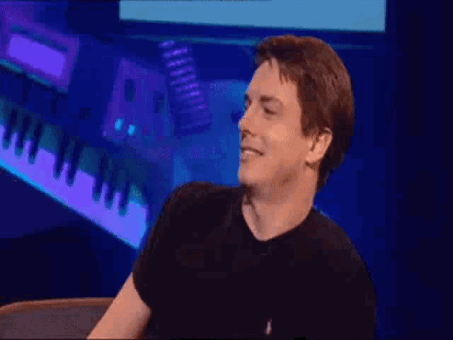 a man in a black shirt is standing on a stage in front of a piano keyboard .