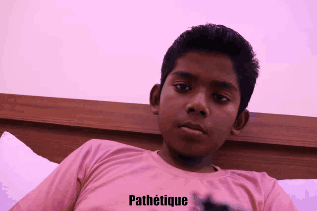 a young boy in a pink shirt is laying on a bed with the word pathetique written below him
