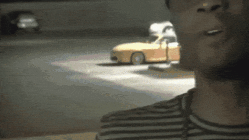 a man in a striped shirt looks at a yellow car in a parking lot