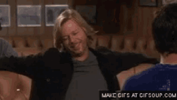 a man is sitting on a couch with his arms outstretched while another man looks on