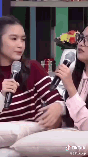 two girls are sitting next to each other holding microphones and talking to each other .